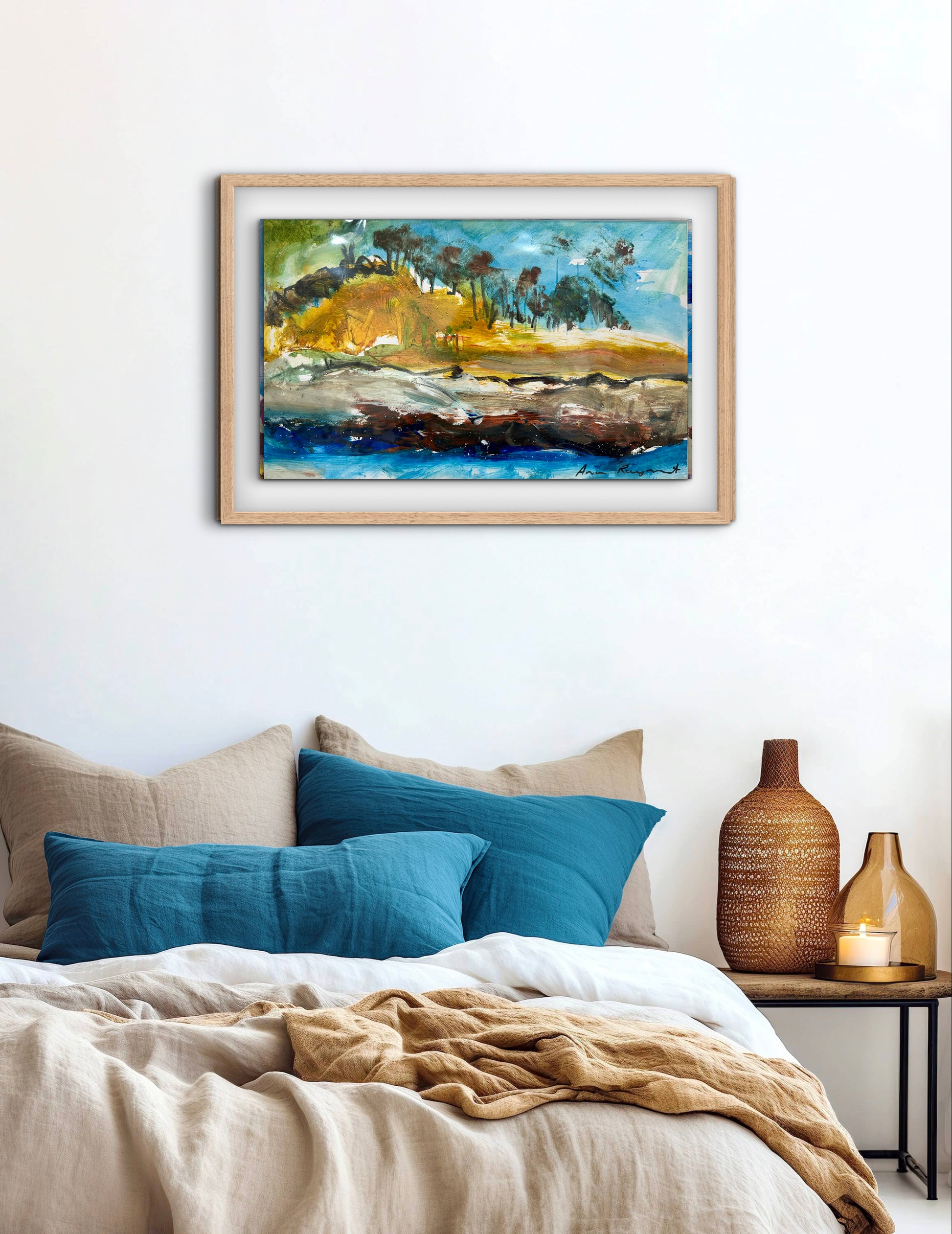 Framed abstract painting above a bed with blue pillows and a wooden nightstand.