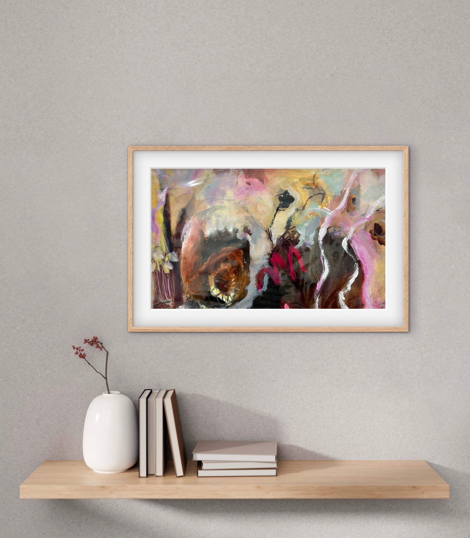 Framed abstract artwork on a wall above a wooden shelf with books and a vase.
